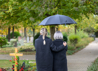Rear view of daughter holding her mother on the way to the man's grave