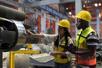 Warehouse of raw materials. Rolls of metal sheet, aluminum material. Male and female factory worker inspecting quality of rolls of galvanized or metal sheet in aluminum material warehouse