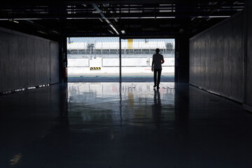 Silhouettes of a man entering a race car racing circuit paddock. - 671122886