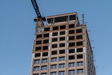 Fototapeta premium A crane and a building under construction against a blue sky background. Builders work on large construction sites, and there are many cranes working in the field of new construction.