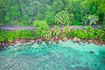Bird eye drone of baie lazare beach, granite stones, turquoise water, coconut palm trees, public road, sunny day, Mahe Seychelles 