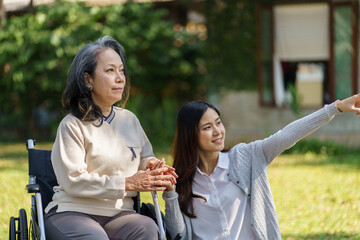 Asian senior woman in wheelchair with happy daughter. Family relationship retired woman sitting on wheelchair in the park age care at retirement home.