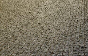 The texture of the paving slab (paving stones) of many small stones of a square shape under bright sunlight