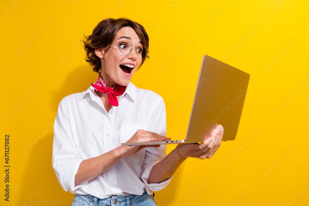 Poster portrait of astonished pretty person open mouth use wireless netbook isolated on yellow color backgr