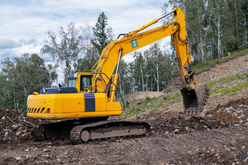 Fototapeta na wymiar A yellow excavator works in the mountains. Construction of roads and houses in beautiful mountains.