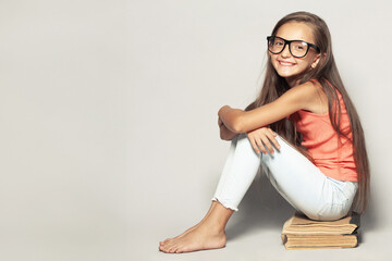 Back to school concept. Portrait of a happy funny girl after itting on bookss over light gray background in summer season casual clothing. Copy-space. Studio shot