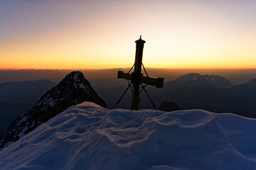 Der atemberaubend schöne Sonnenaufgang mit Schnee im Winter am Gipfelkreuz der Watzmann Südspitze