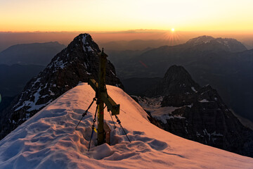 Der atemberaubend schöne Sonnenaufgang mit Schnee im Winter am Gipfelkreuz der Watzmann Südspitze