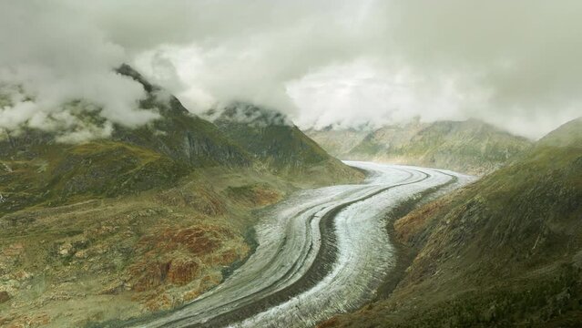 Aerial shot over Swiss Aletsch Glacier below low hanging clouds. Early autumn morning.