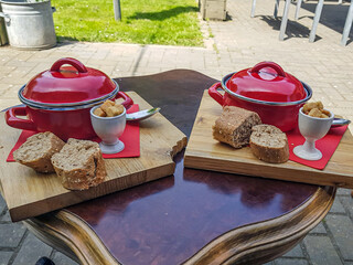 Table with two red pot with mustard soup accompanied with slices of bread and croutons on a wooden board, sunny day for lunch in garden, grass and sunlight in blurred background