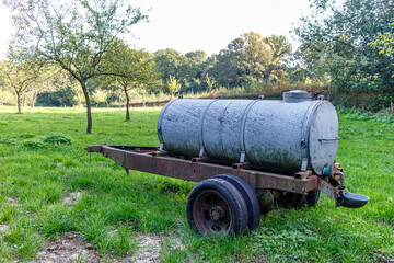 Old mobile water tank or waterer for livestock on an agricultural plot on Dutch farm, trees with green foliage in background, sunny day in Sweikhuizen, South Limburg, Netherlands