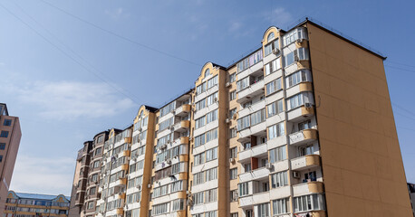 Old residential apartment building with windows, balconies and air conditioners against a blue sky.