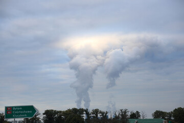 Ogromne kłęby dymu z kominów elektrowni oświetlone przez słońce nad chmurami.