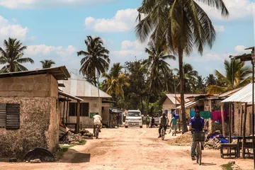Zelfklevend Fotobehang African road through village people going about business © Elena