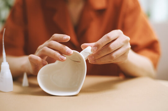 Hands of woman glueing handle to heart shape coffee cup