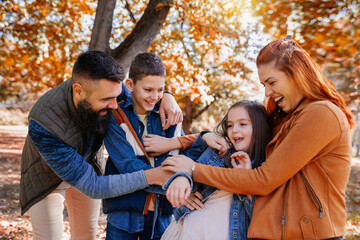 Parents tickle their children. Sunny autumn day in the colorful park - obrazy, fototapety, plakaty