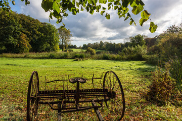 Eine verrostete landwirtschaftliche Maschine auf einer grünen Wiese im sonnigen Herbst vor einer historischen Schmiede