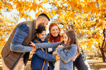 Parents tickle their children. Sunny autumn day in the colorful park - obrazy, fototapety, plakaty