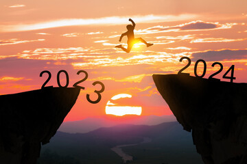 Greetings and have a great Christmas and new year in 2024.silhouette of a man leaping from a cliff in 2023 to one in 2024 under a cloudy and sunny sky. - obrazy, fototapety, plakaty