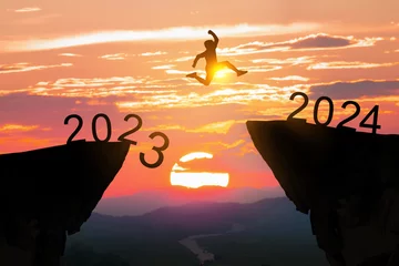 Fotobehang Greetings and have a great Christmas and new year in 2024.silhouette of a man leaping from a cliff in 2023 to one in 2024 under a cloudy and sunny sky. © chartphoto