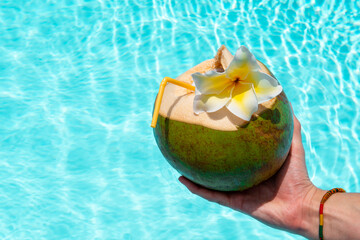 Coconut in hand over against swimming pool. Summer vacation at Koh Samui.