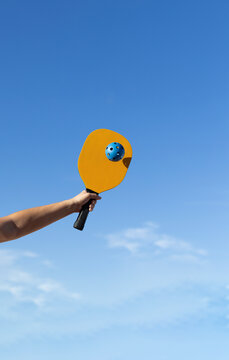 Arm with yellow pickleball paddle and blue ball