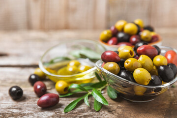 A set of green, red and black olives on  background. Various types of olives in bowls and fresh olive leaves. Vegan. Olive fruits. Place for text. Copy space. - obrazy, fototapety, plakaty