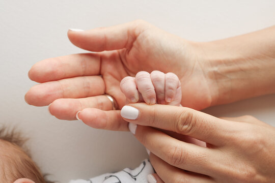 Parents' hands hold the fingers of a newborn baby. The hand of a mother and father close-up holds the fist of a newborn baby. Family health and medical care. Professional photo on white background