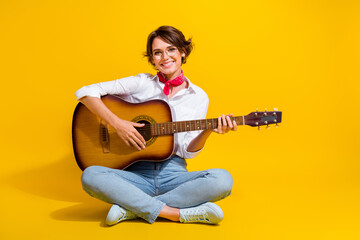Photo of lovely adorable girl wear stylish clothes sit floor play guitar acoustic instrument isolated on yellow color background