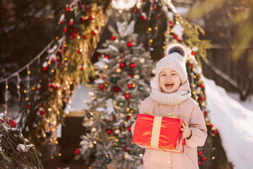 Little girl with a Christmas gift outdoors in winter on Christmas Eve. New Year background for holiday sale or promotion.