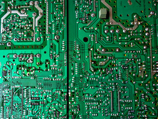 A close-up image of a green circuit board with various silver and gold components. Green computer circuit board as a background. Chip.