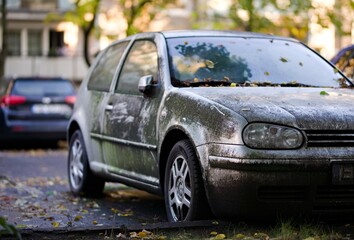 Porzucone srebrne auto pokryte brudem i mchem stojące na osiedlowym parkingu w mieście