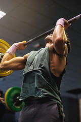 Strong muscular man doing exercises with barbell in gym