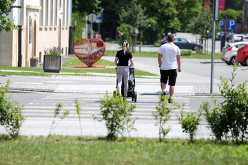 Kobieta z wózkiem i mężczyzna przechodzą przejściem dla pieszych.