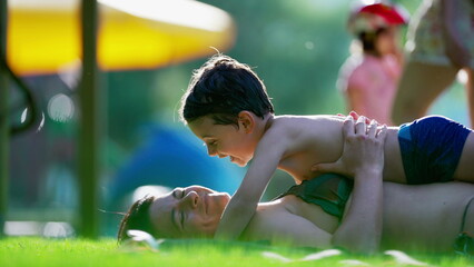 Candid loving moment between mother and child laid on grass during summer day activity, little boy wanting to kiss mom, authentic tender moment - obrazy, fototapety, plakaty