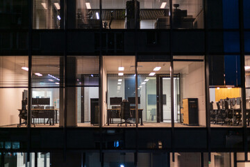 Business building with office and workspaces with desks, laptops and armchairs at night. Work,...