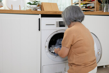 back view senior woman doing laundry with washing machine at home