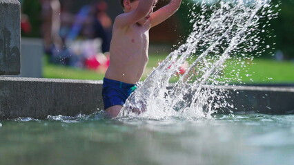 Happy child splashing water at outdoor pool in slow-motion. Little boy throwing water in the air with hand in 120fps during summer day