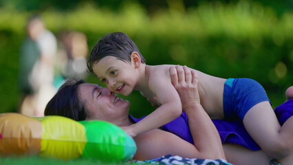 Happy mother and child laying down in outdoor grass after swimming at pool. Little boy and mom...