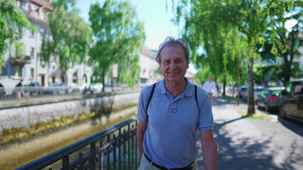 Happy senior man strolling in urban street during bright beautiful day. Relaxed elderly retired person walking in city sidewalk