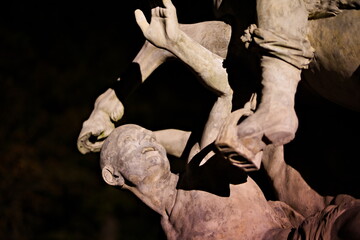 Zbliżenie na detal pomnika - głowę mężczyzny oraz kopyto konia w parku miejskim wieczorem,...