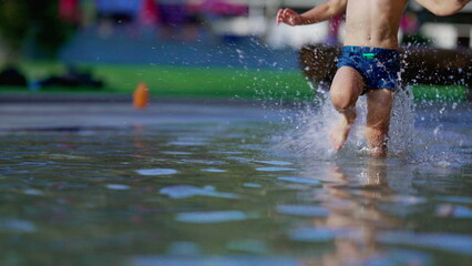 Joyful child running in swimming pool water splashing water in slow-motion during summer day. Active little boy sprinting at 120fps