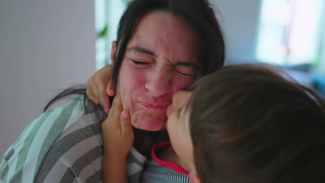 Energetic child kissing mother in cheek with rough embrace. Excited son warm loving embrace kisses mom energetically