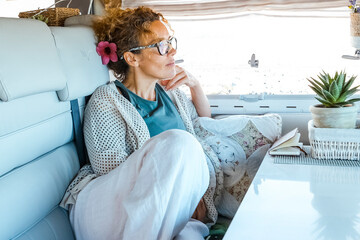One woman relaxing inside camper van motorhome looking outside the view from the window. Traveler and freedom independence people female lifestyle. Interior of rv vehicle and lady having relax serene