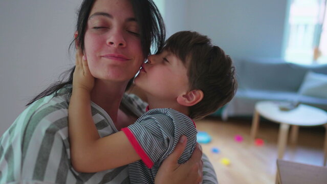 Energetic child kissing mother in cheek with rough embrace. Excited son warm loving embrace kisses mom energetically