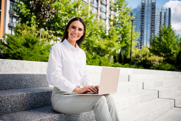 Photo of cheerful adorable lady dressed stylish clothes sitting on stairs enjoying sunny warm autumn days outside