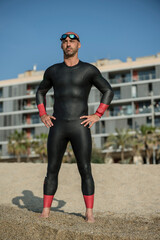 Confident man wearing a wetsuit standing in the shore ready for swimming. Professional athlete...