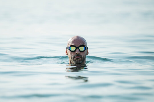 Confident Man Swimming In The Ocean Wearing Glasses Looking At Camera. Swimmer Pulling His Head Out Of The Water Focused.