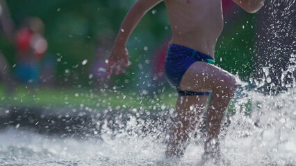 Happy child running in swimming pool water in slow-motion during summer day. Active little boy splashing water runs forward in 120fps