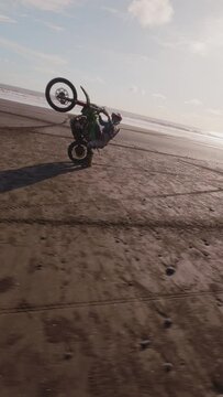 Vertical video. Professional sportsman enduro motorcycle driving sandy tropical beach extreme tricks riding one back wheel. Man biker enjoying dangerous riding wheely bike nature aerial FPV drone view